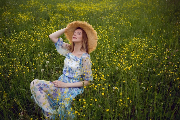 花のドレスと麦わら帽子の美しい女性が午後に畑に座っています