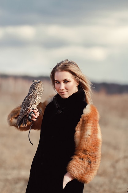 Beautiful woman in a fur coat with an owl on his arm.