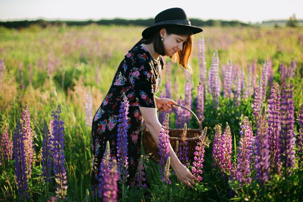 Photo beautiful woman gathering lupine in rustic basket in sunny field relaxing in summer countryside