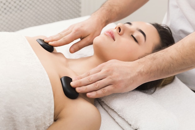 Beautiful woman getting hot stones shoulders massage in spa salon. Beauty treatment therapy, wellness and relaxation concept