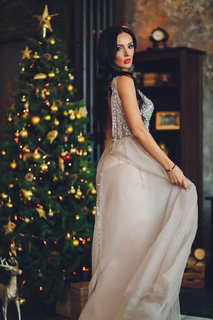 Красивая женщина девушка в новогодней студии позирует, фото новогодняя фотосессия. Красивая девушка в роскошном платье со стройными ножками. Рождество, зима, концепция счастья.