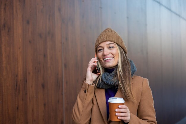 Bella donna che va a lavorare con il caffè che cammina vicino all'edificio per uffici ritratto di donna d'affari di successo che tiene una tazza di bevanda calda