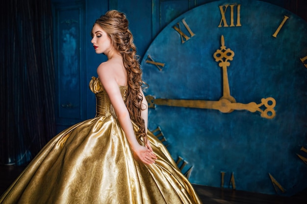 Beautiful woman in a golden ball gown in the great blue interior