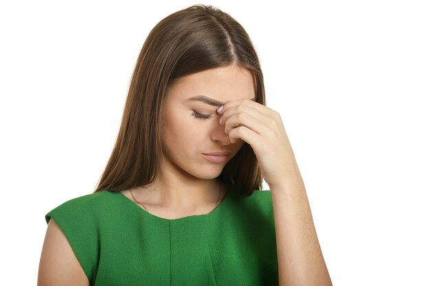 Beautiful woman in green dress with headache on white background