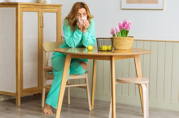 Foto una bella donna con un vestito verde da casa siede in cucina al tavolo e beve il tè