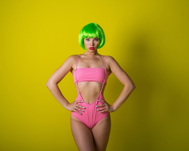 Beautiful woman in a green short wig and pink bikini posing on a yellow background portrait of a girl with sensual red lips