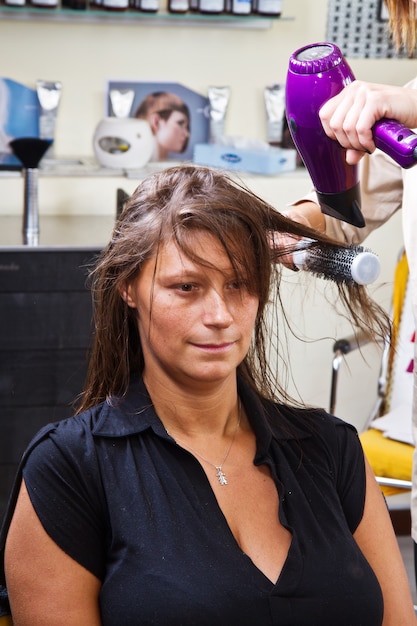 Красивая женщина в парикмахерской сушит волосы феном