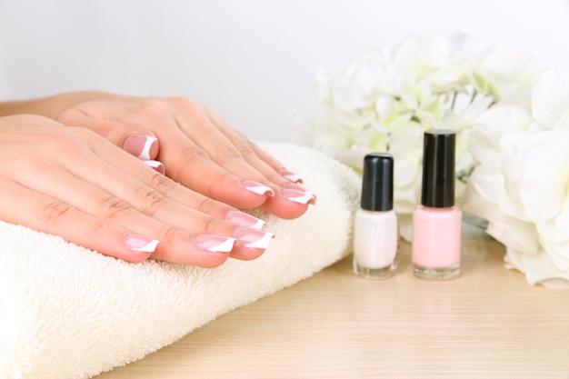 Beautiful woman hands with french manicure and flowers on table on white background