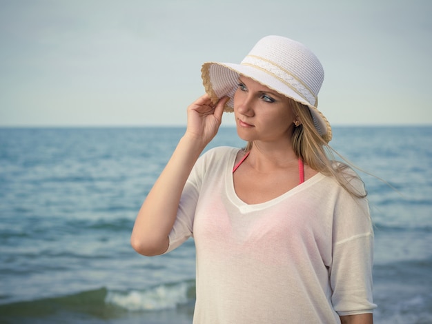 夜の海に対する帽子の美しい女性。