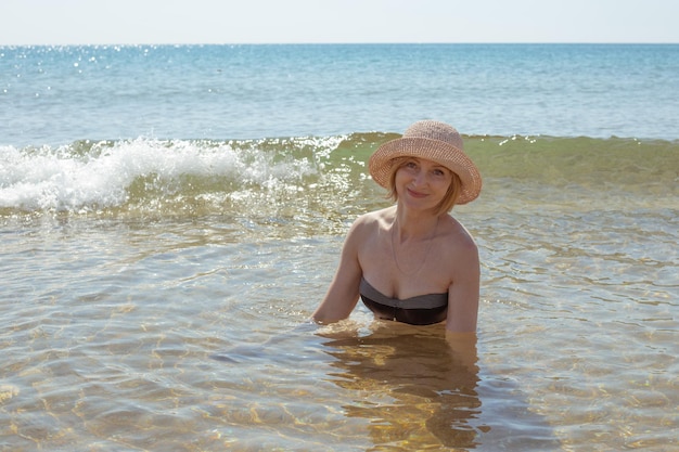 笑顔の海の水の帽子とビキニの美しい女性。夏の娯楽とリラクゼーション。