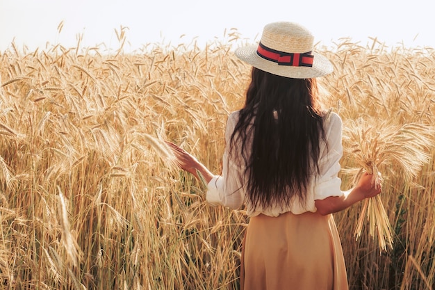 Photo beautiful woman in a hat and dress in a wheat field.