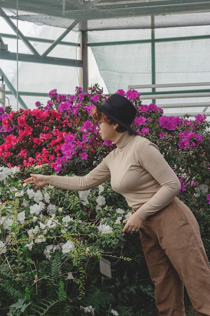 A beautiful woman in a hat laughs among the green plants of greenhouse