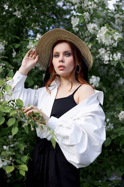 Beautiful woman in a hat in spring in the branches of flowering Apple bushes