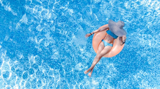 위에서 내려다본 수영장 공중 꼭대기에서 모자를 쓴 아름다운 여성, 어린 소녀는 링에서 휴식을 취합니다