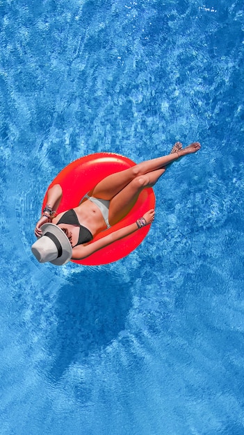 Beautiful woman in hat in swimming pool aerial view from above, young girl relaxes and has fun on inflatable ring