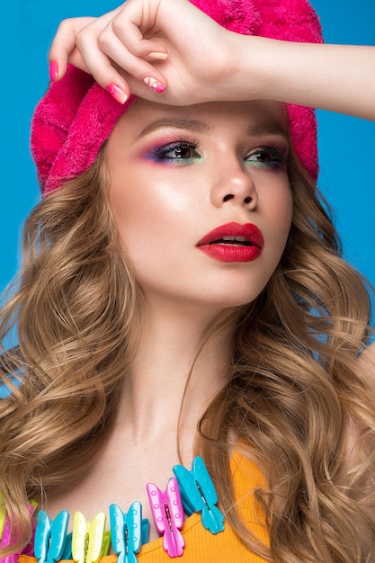 Beautiful woman in a hat with colorful makeup curls and pink manicure