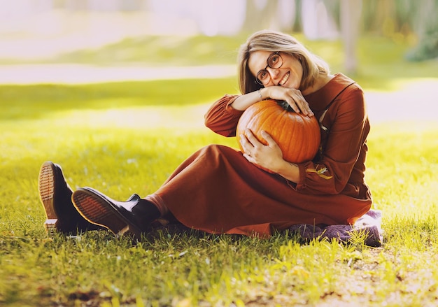 아름 다운 여자는 호박과 함께 포즈를 취하는 긴 갈색 드레스 소녀를 입고 가을 공원에서 포즈를 취하는 여가를 가지고 있습니다.