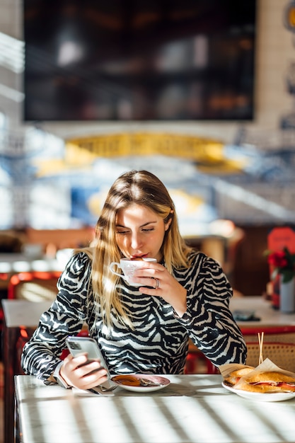 携帯電話を使用してレストランで朝食を持っている美しい女性。