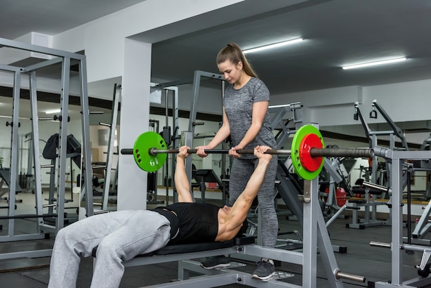 Beautiful woman helping men to lift dumbbell