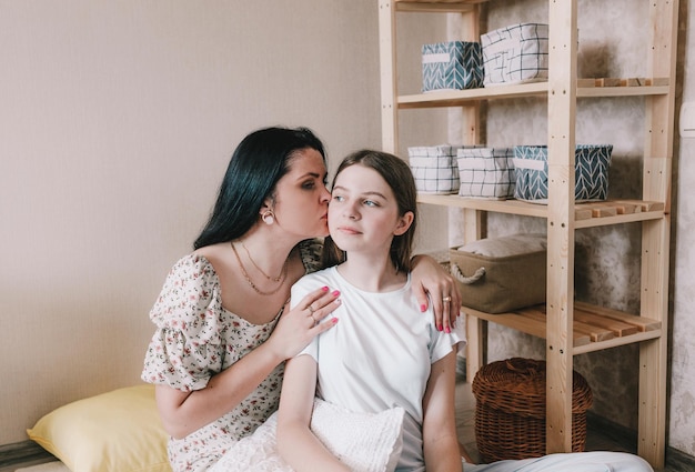 A beautiful woman and her sweet little daughter hang and smile while sitting on the floor, mom kisses her daughter on the cheek