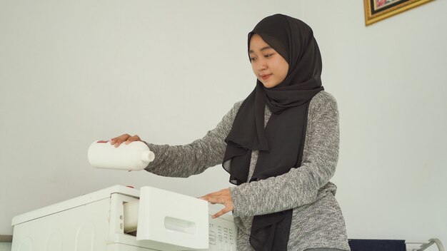 Beautiful woman in hijab pours detergent for her laundry at home