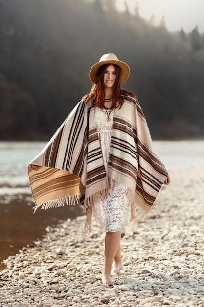 Beautiful woman hipster walking on river beach in mountainssmiling and enjoying boho travel concept