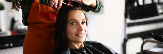 Beautiful woman hold strand of hair and cut bang with scissors at workplace