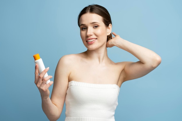 Beautiful woman holding bottle with hair shampoo or shower gel isolated on blue background