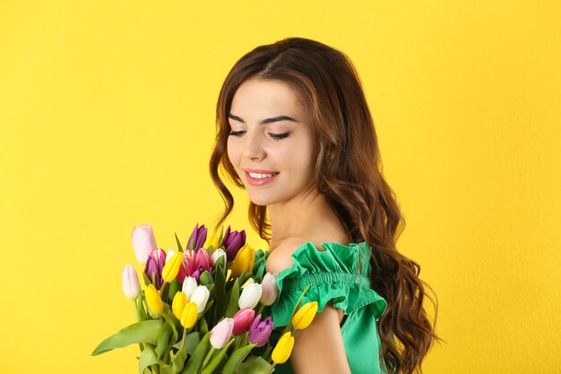 Beautiful woman holding bouquet of tulips on color background