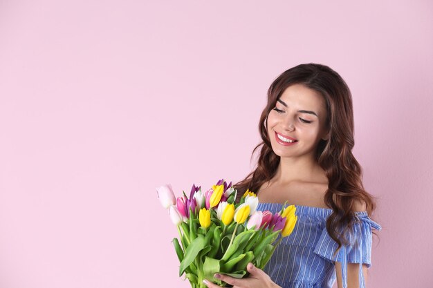 Beautiful woman holding bouquet of tulips on color background