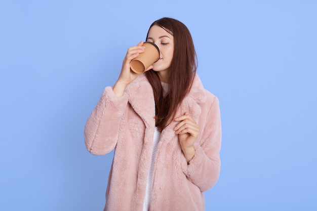 Beautiful woman holding disposable mug, drinking hot beverage