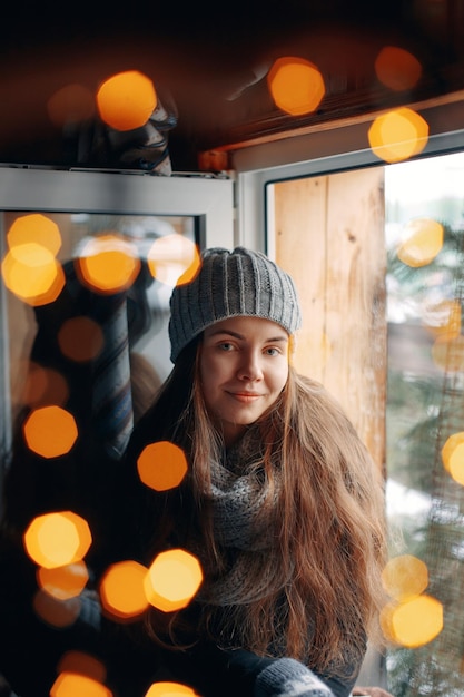 Beautiful woman holding and drinking a cup of coffee or cocoa in gloves sitting home by the window