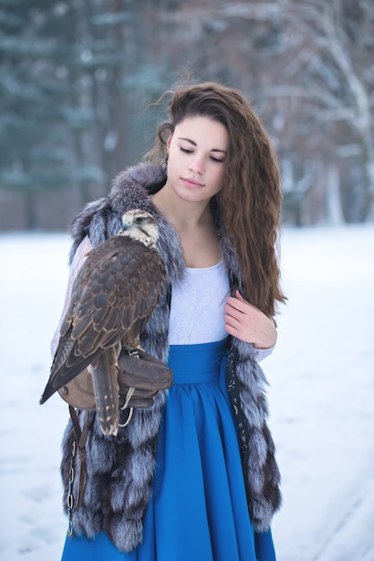 Beautiful woman holding a falcon on her hand in winter