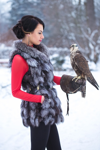 Bella donna che tiene un falco sulla sua mano in inverno