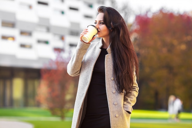 紙のコーヒーカップを押しながら街の散歩を楽しんで美しい女性