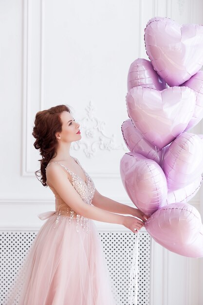 Beautiful woman holding pink balloons heart shaped. Model female on st. Valentine`s background.