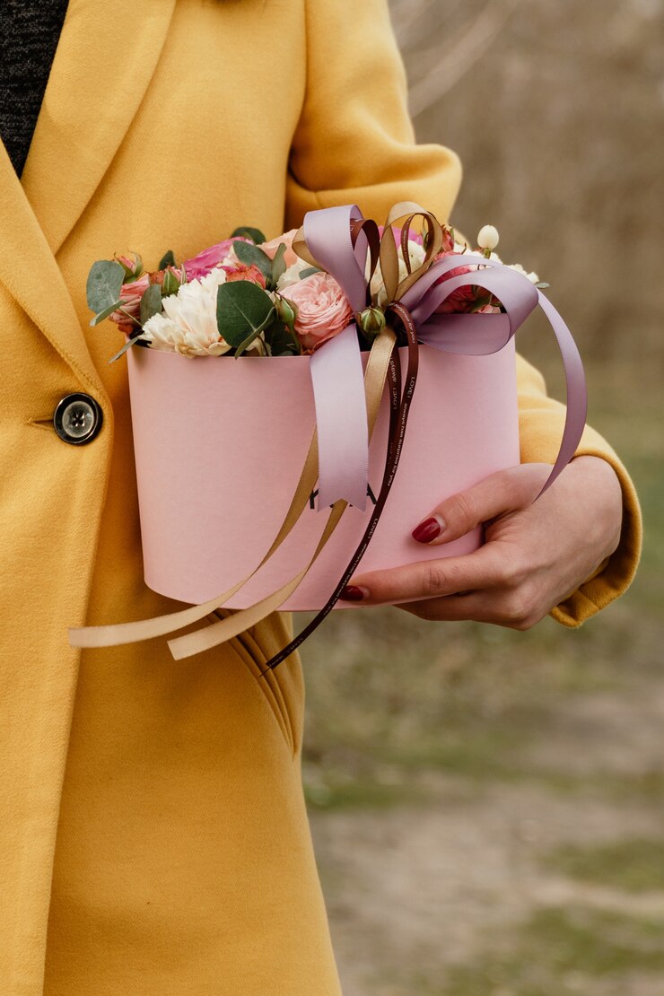 美しい女性の花とピンクのボックスを保持しています。女性の日への贈り物。
