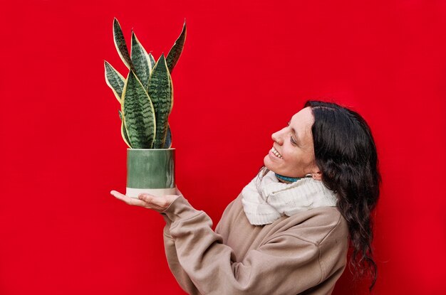Photo a beautiful woman holding a pot with snake plants on red wall