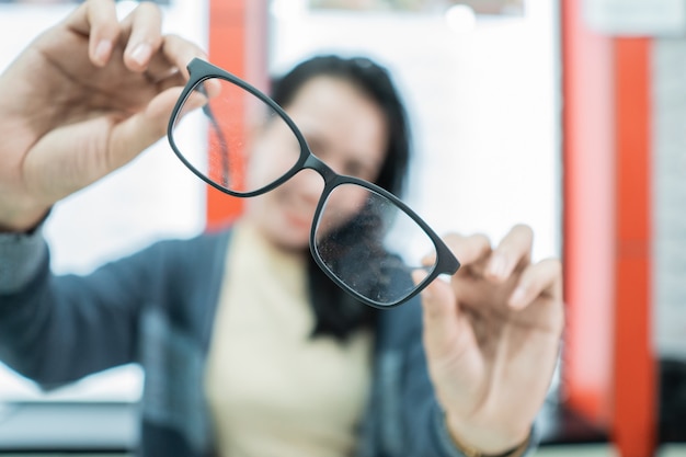 A beautiful woman holding a sample of glasses in an eye clinic against an eyeglass display window