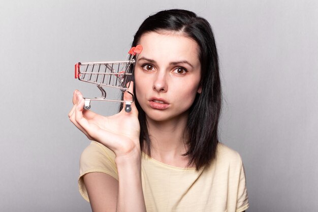 Foto bella donna che tiene in mano un piccolo carrello del supermercato un simbolo dello shopping