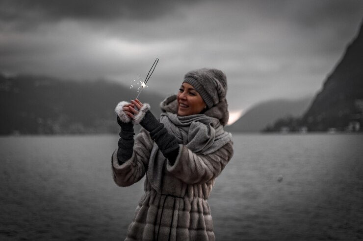 Photo beautiful woman holding sparkler against sky during winter