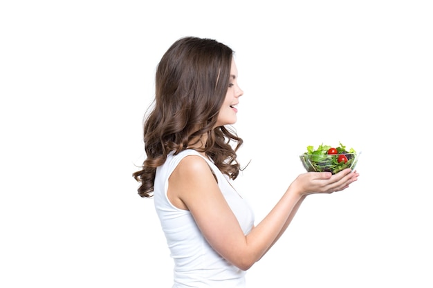 Beautiful woman holding transparent bowl with healthy salad meal, looking at bowl, over white, with copy space. Healthy lifestyle.