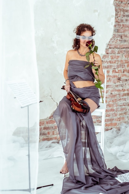 Beautiful woman holding a violin and smelling red rose