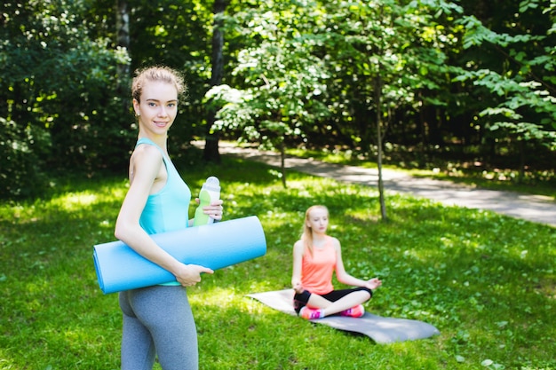 Bella donna che tiene una stuoia e una bottiglia di acqua di yoga.