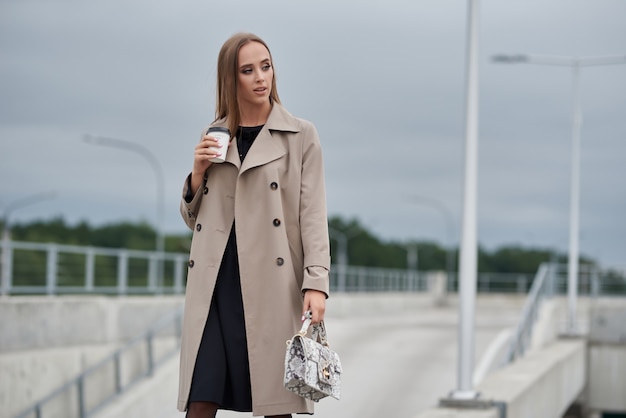 Beautiful woman holds coffee to go. woman holding cup of hot drink In hand, walking on street