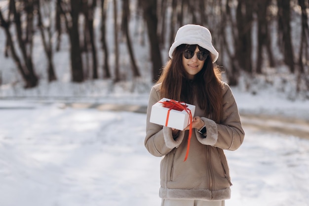 美しい女性は、冬の通りで弓で箱に包まれた贈り物を手に持っています