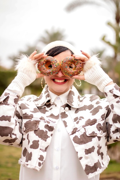 A beautiful woman holds two donuts and puts them on her eyes and she is happy