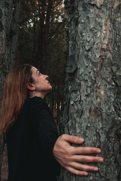 Foto la bella donna che abbraccia e tocca gli alberi nella foresta autunnale