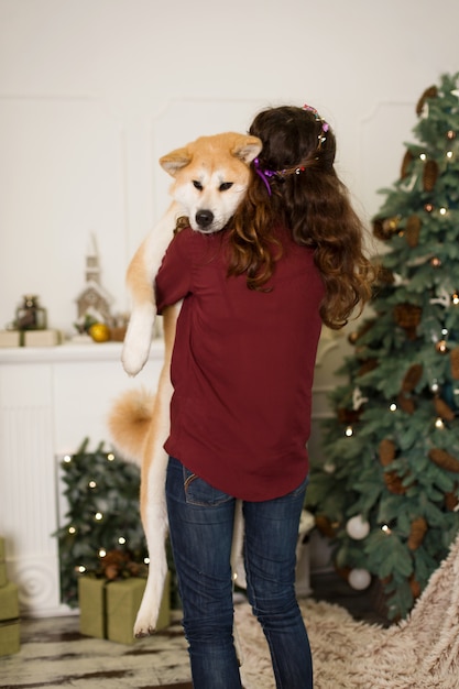 Beautiful woman hugs, cuddles with her akita inu dog. on a background of a Christmas tree dresser with candles in a decorated room. happy new year and merry christmas