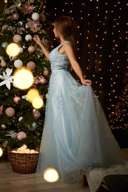 写真 青いイブニングドレスの美しい女性がクリスマスツリーを飾る